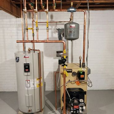 A neatly installed boiler and water heater system with copper piping in a basement.