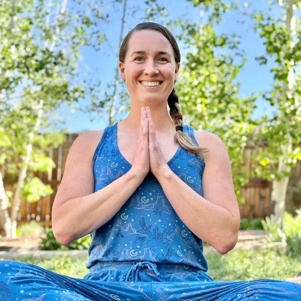 Woman in blue outfit practicing yoga outdoors with hands in prayer pose.
