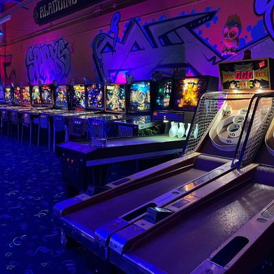 Dimly lit arcade with pinball machines and skee-ball lanes under neon lights.