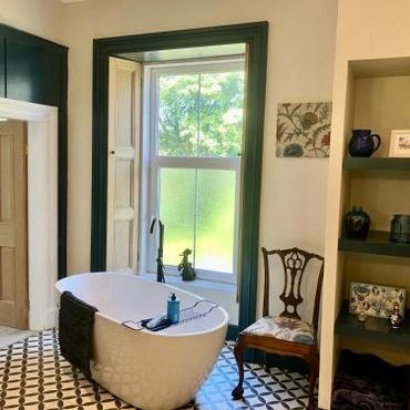 Elegant bathroom with a freestanding tub and vintage chair by a large window.
