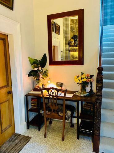Cozy wooden desk setup with a mirror, flowers, and a chair by the staircase.