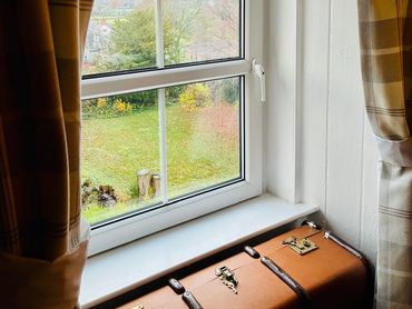 View through a window with plaid curtains and a vintage suitcase on the sill.
