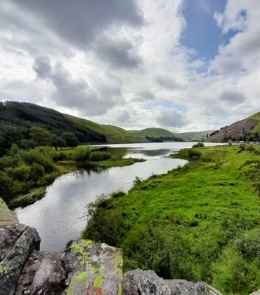 A calm river flowing through lush green hills under a cloudy sky.
