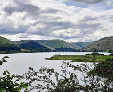 A scenic lake with sailboats and green hills under a cloudy sky.