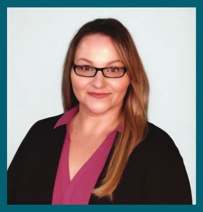 Professional woman with glasses smiles confidently against a plain background.