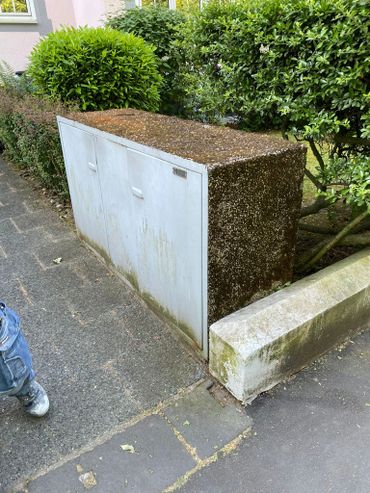 Weathered outdoor utility box next to a hedge and sidewalk.
