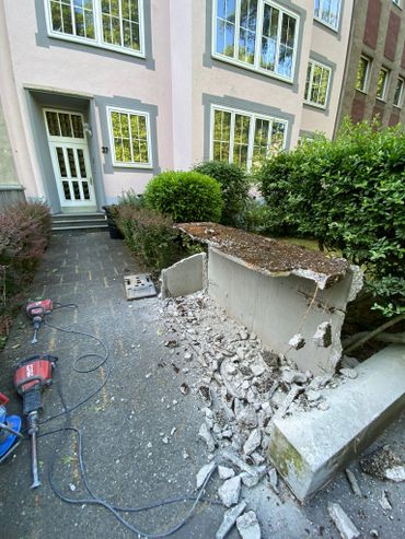 Demolition of a concrete structure near a residential building with tools scattered on the ground.