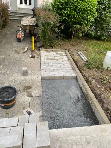 Paving stones being laid for a garden path with tools and materials nearby.
