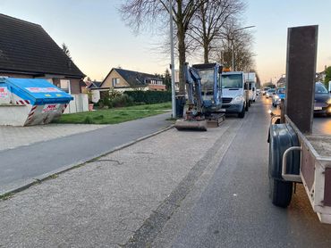 A small excavator and trucks parked along a street in a residential neighborhood.