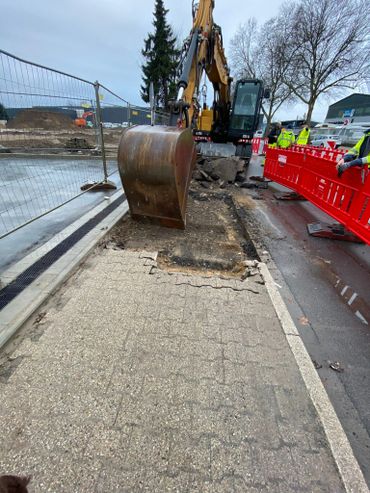 Construction site with excavator digging up pavement and workers nearby.
