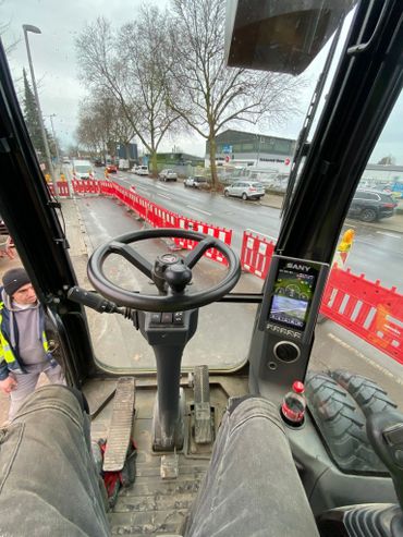 View from a construction vehicle cab showing steering and controls on a rainy day.