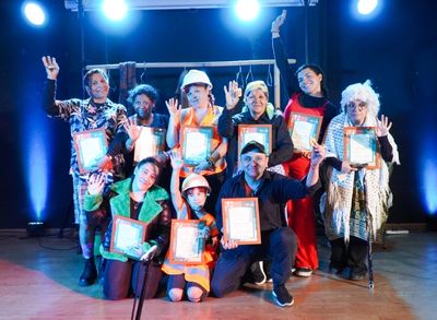 Group of diverse people holding certificates and waving on stage under bright lights.