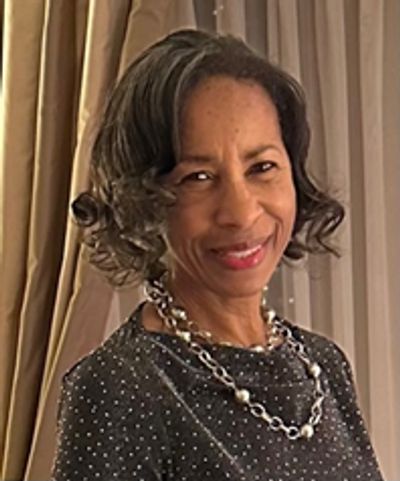 Woman smiling warmly in a polka dot dress with a statement necklace.