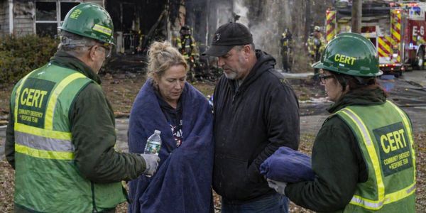 CERT volunteers assist fire victims wrapped in blankets at a fire scene.