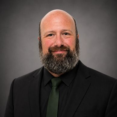 Professional portrait of a bald man with a beard in a black suit and green tie.