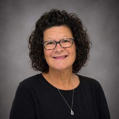 Smiling woman with curly hair and glasses wearing a black top and necklace.