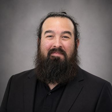 Man with a full beard and black suit smiling at the camera.