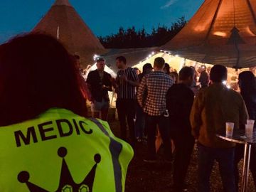 Event medic standing facing a number of customers at festival with a large teepee in the background.