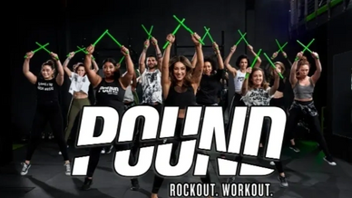 Group exercising with green drumsticks in a Pound workout class.