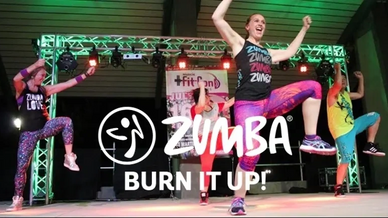 Energetic group Zumba dance class on stage with colorful outfits and vibrant lighting.