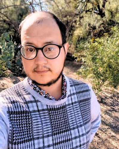 Man wearing glasses and a checkered sweater outdoors.