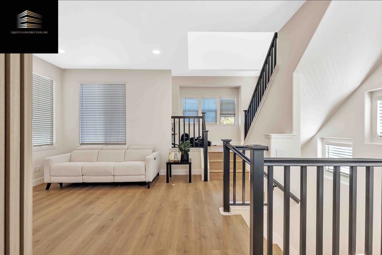 Modern living space with beige sofa, wooden flooring, and black stair railings.
