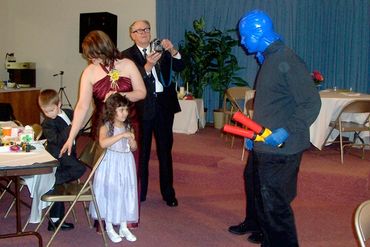 a blue man interacts with a young girl and wants while grandpa takes a picture