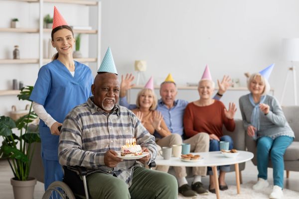 Elderly man in wheelchair celebrating birthday with friends and nurse.