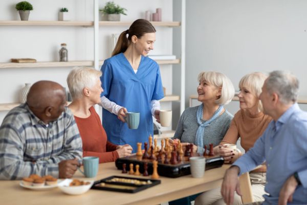 Nurse serving drinks to elderly friends playing chess.