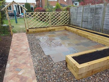 A newly landscaped backyard with a tiled patio and wooden planters.