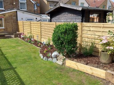 A well-maintained garden with a green lawn, flowerbed, and wooden shed.