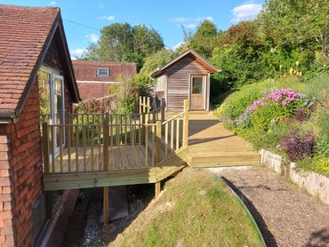 Wooden deck and shed in a sunny garden with blooming flowers.