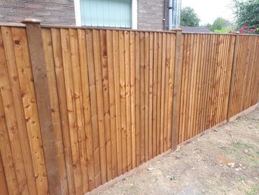 A newly installed wooden fence in a backyard beside a brick house.