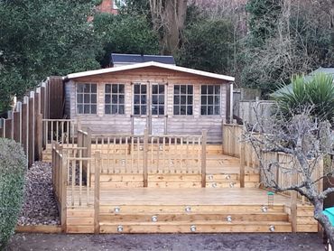 A wooden garden shed with a tiered wooden deck and railings.