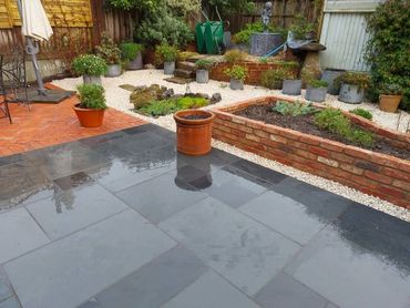 A wet garden patio with potted plants and a raised brick flower bed.