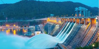 Hydroelectric dam releasing water against a mountain backdrop at dusk.