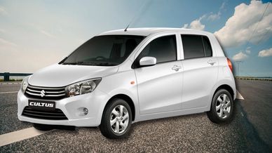 White Suzuki Cultus hatchback parked on a road under a blue sky.