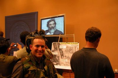 Mike Pierson standing in front of screen showing Saddam Husein after capture in 2003.
