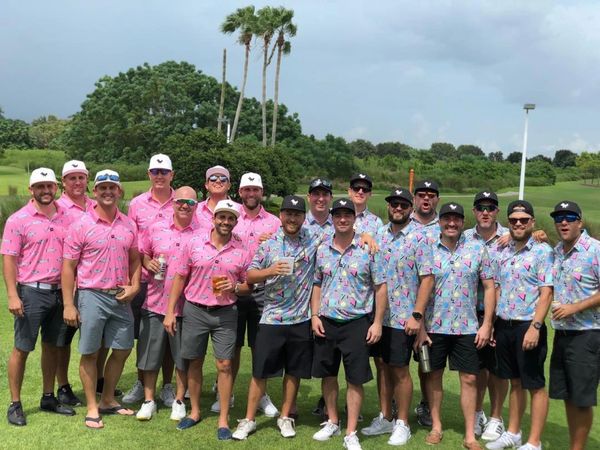 Two groups of men in matching colorful golf shirts posing outdoors.