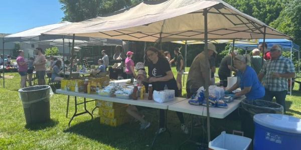 People serving food under tents at an outdoor event on a sunny day.