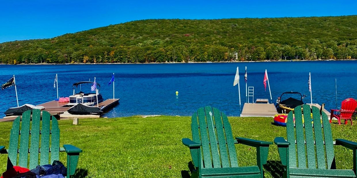 Green Adirondack chairs by a lake with docks and a wooded hill in the background.