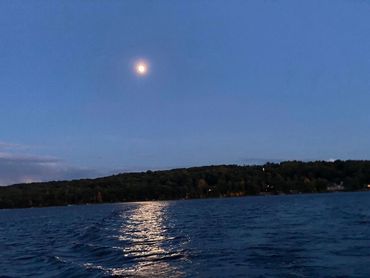 Moonlight reflecting on calm lake water with forested shoreline in the background.