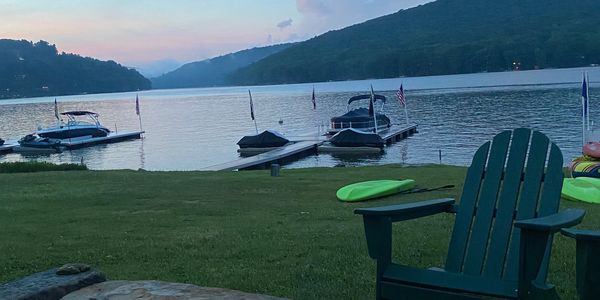 Empty Adirondack chairs by a peaceful lakeside dock at dusk.