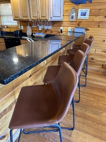 Brown leather bar stools lined up along a granite countertop in a wooden cabin kitchen.