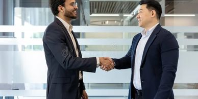 Two businessmen in suits shaking hands in an office setting.