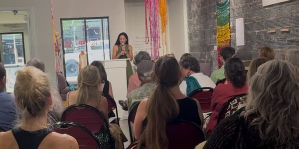 Woman speaking at a podium to an audience indoors.