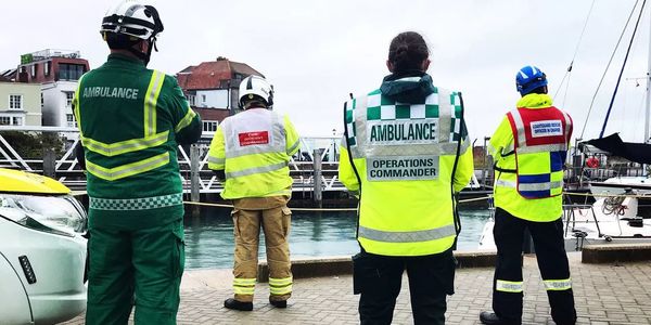 Emergency responders from ambulance, fire, and coastguard stand by a waterfront.