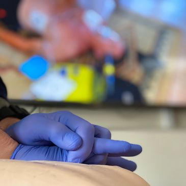 Person wearing blue gloves practicing CPR on a training mannequin.