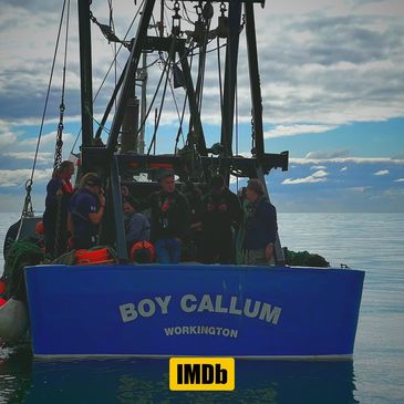 Fishermen aboard the Boy Callum boat on calm waters under a cloudy sky.
