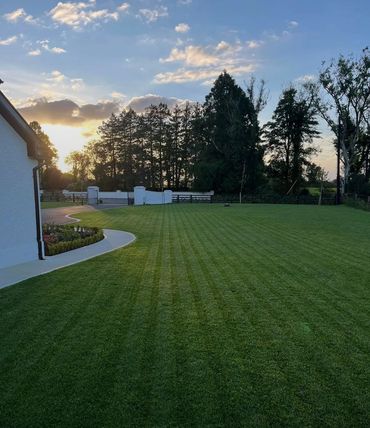 Sunset over a neatly mowed lawn beside a house and trees.
